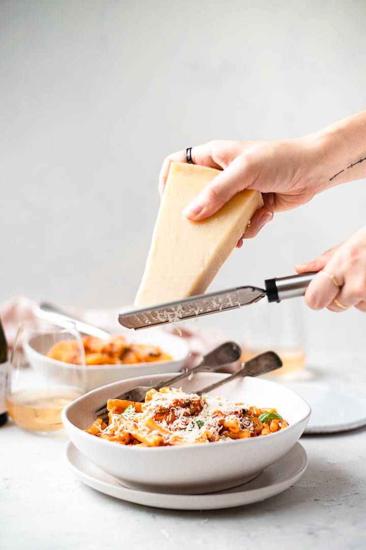 Grating parmigiano reggiano over the top of a bowl of vodka tomato pasta
