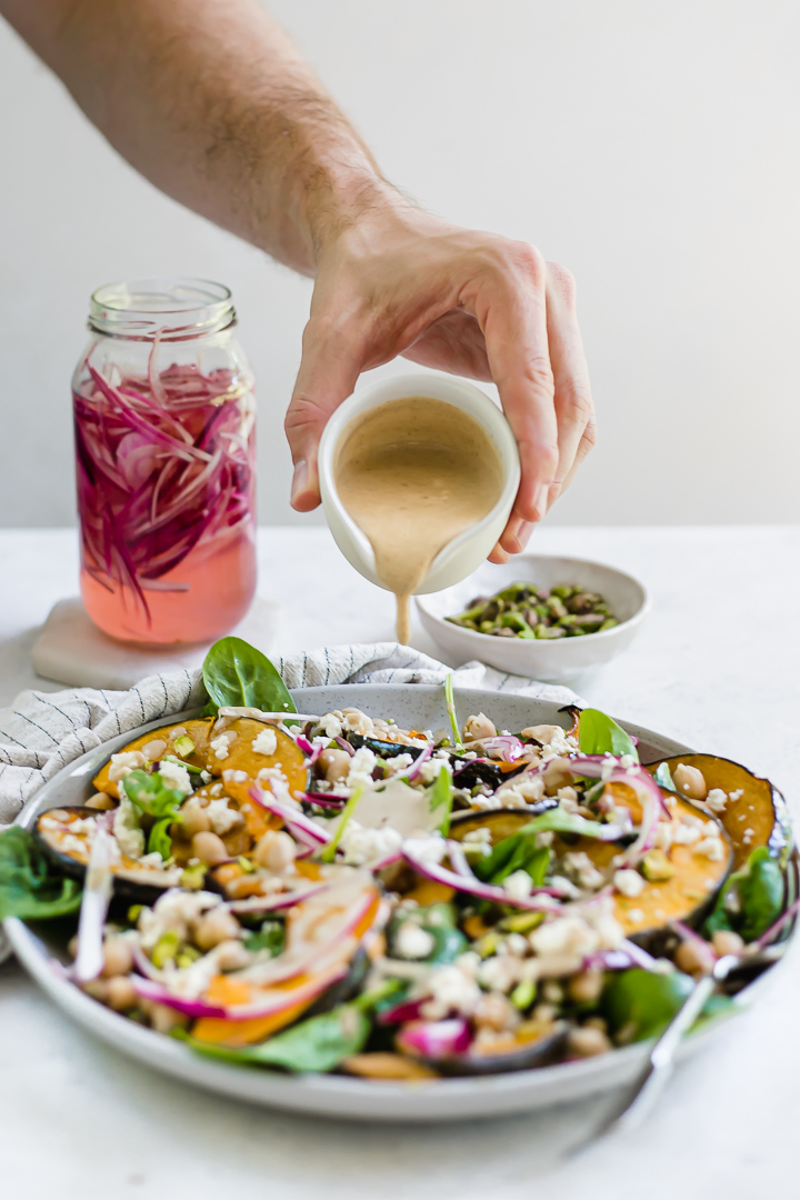 Pouring tahini dressing over pumpkin and chickpea salad