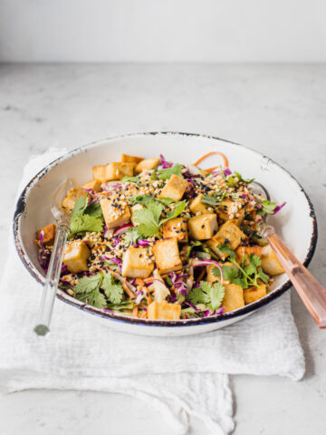 A bowl of satay slaw with crispy tofu and serving tongs