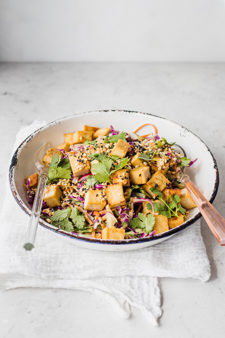 A bowl of satay slaw with crispy tofu and serving tongs