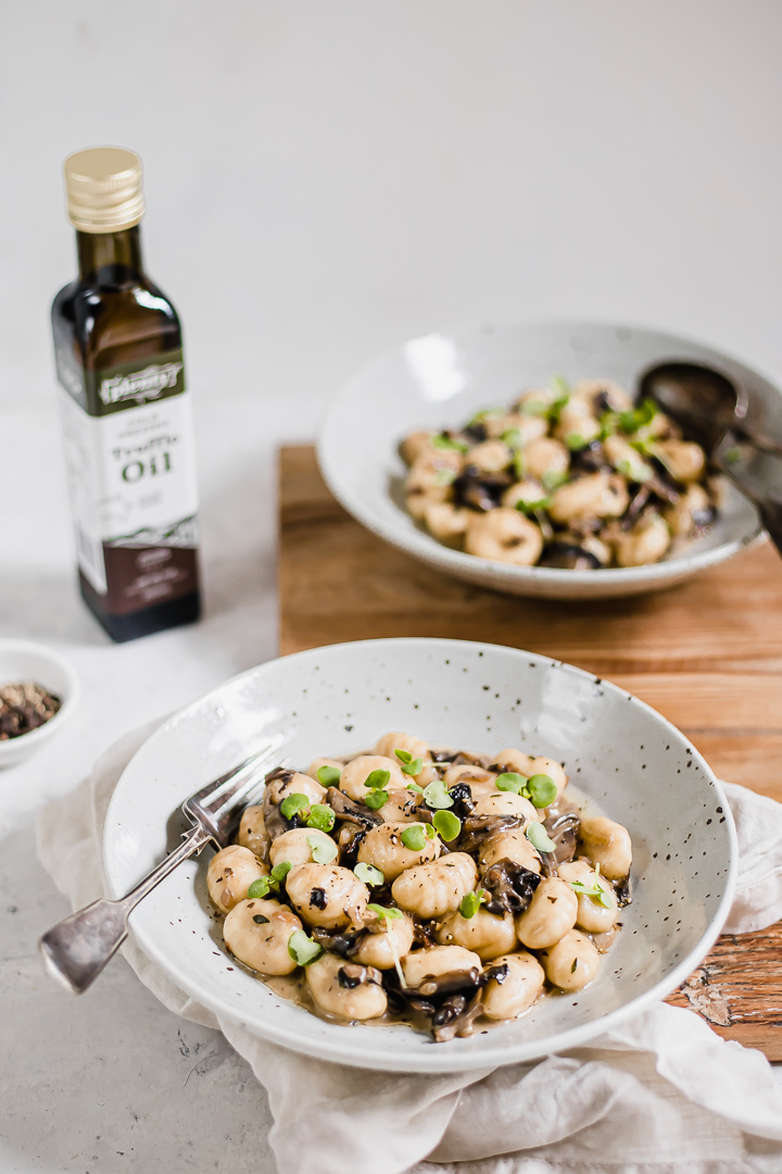 A bowl of mushroom gnocchi with a bottle of truffle oil in the background
