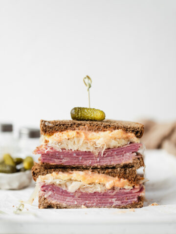 A front on shot of a Reuben Sandwich with a gherkin skewered on top