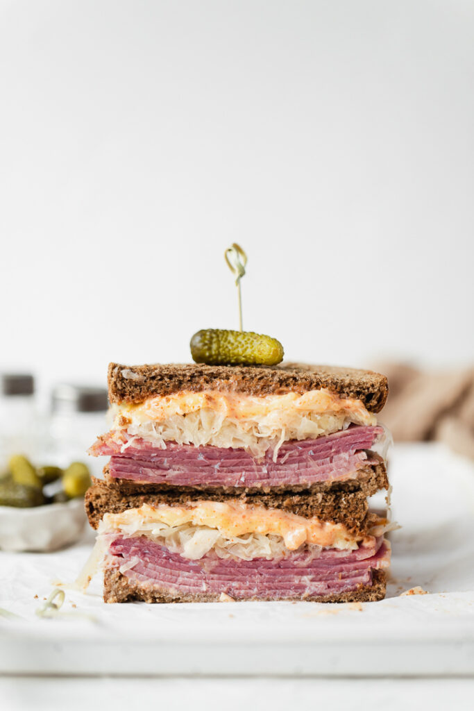 A front on shot of a Reuben Sandwich with a gherkin skewered on top