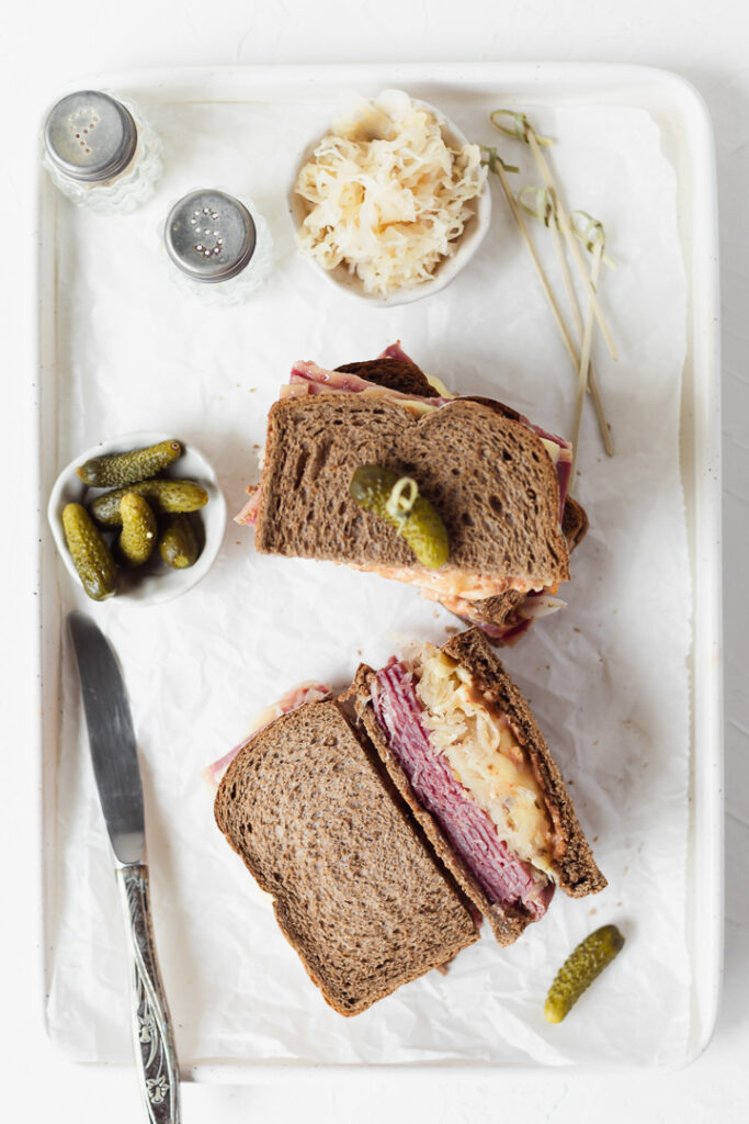 Top down view of two Reuben sandwiches on a tray with sauerkraut and gherkins