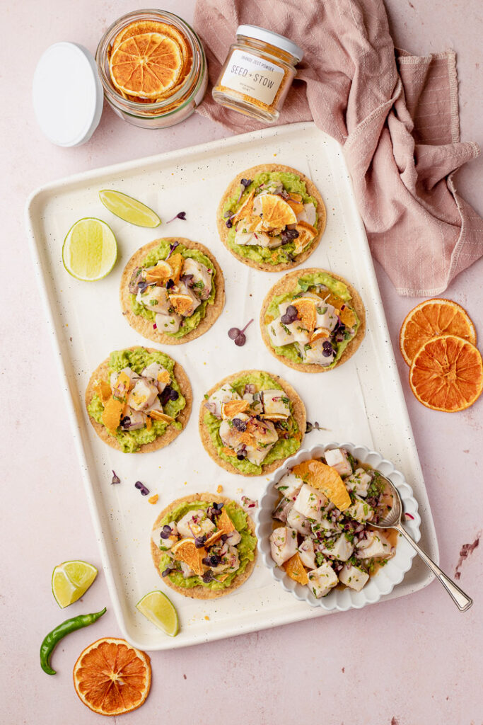 Six tostadas on a white tray with a bowl of king fish ceviche