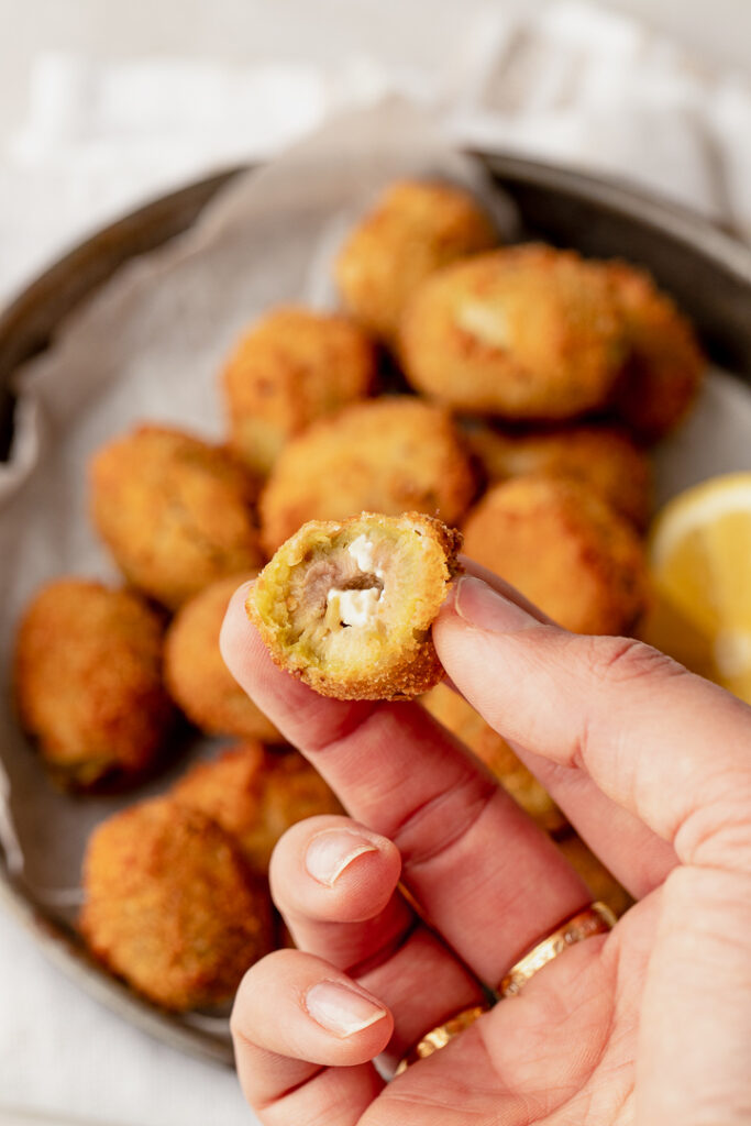 A hand holding a fried stuffed olive with a bite out of it showing the Danish feta on the inside.