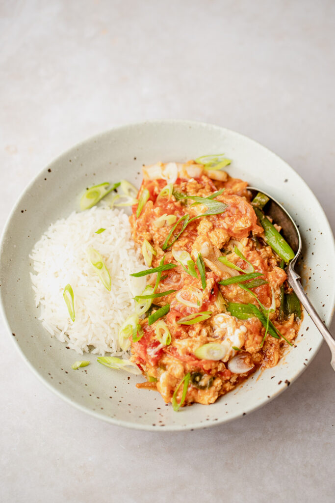 A bowl of tomato egg stir fry with rice and a spoon