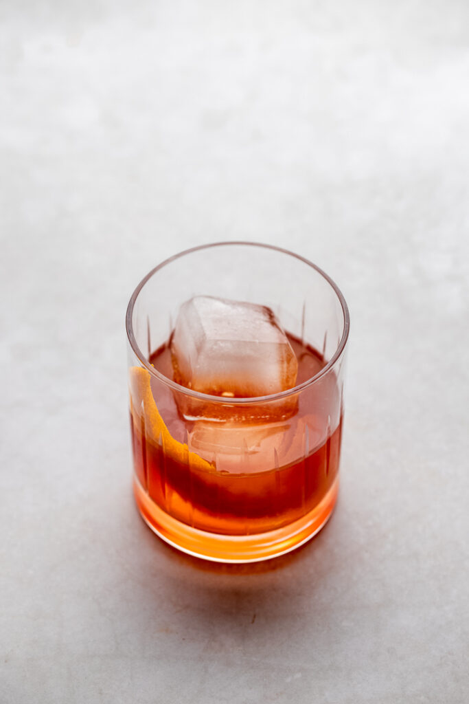 A rocks glass with an amber liquid and an orange twist, the treacle cocktail