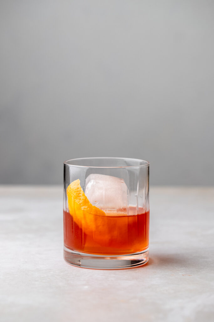 A rocks glass with an amber liquid and an orange twist, the treacle cocktail