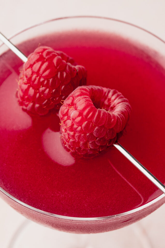 Close up of raspberries garnishing a gin & jam cocktail