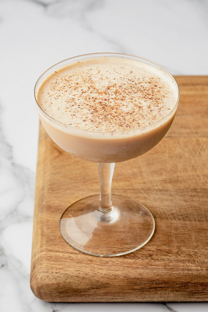 Brandy Alexander cocktail in a coupe glass sitting on a wooden board
