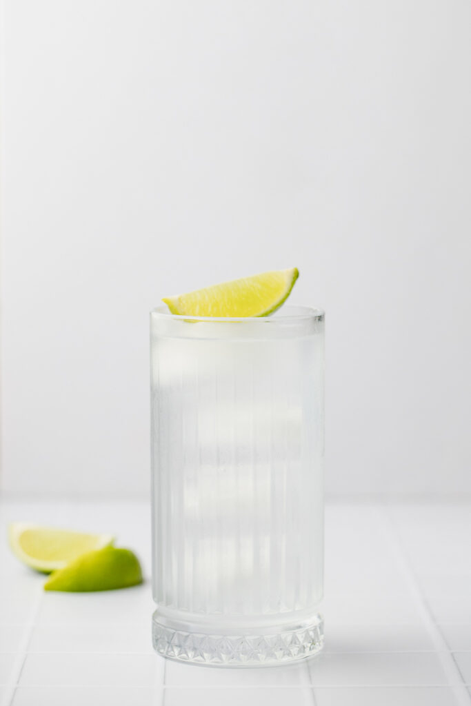 A front on shot of a collins glass with a clear liquid inside and a wedge of lime on top.