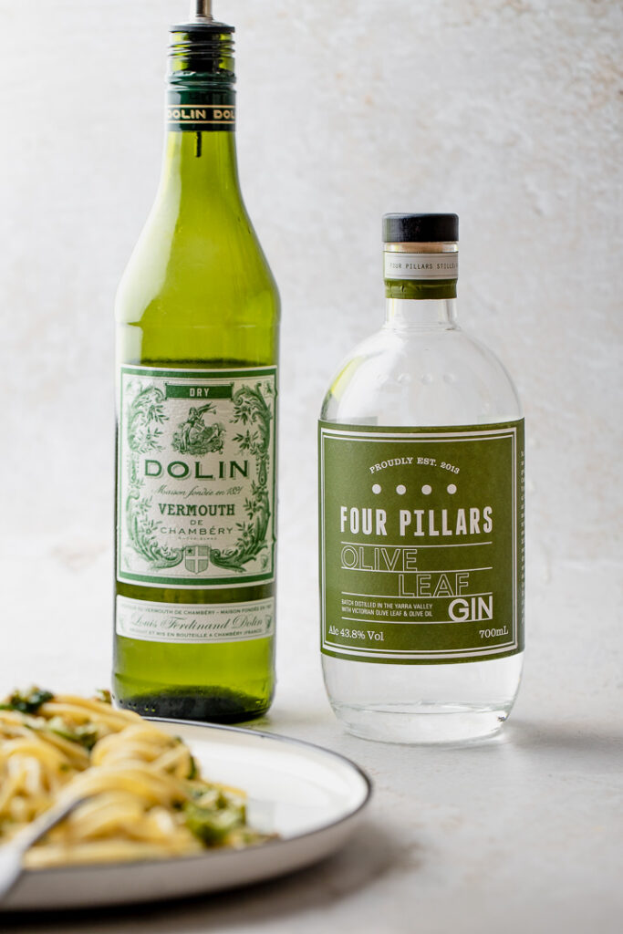 A bottle of dry vermouth and gin next to a plate of pasta.