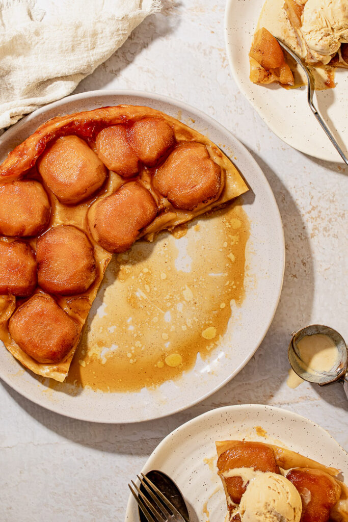 Apple tarte tatin with two slices cut an on separate plates, topped with ice cream.