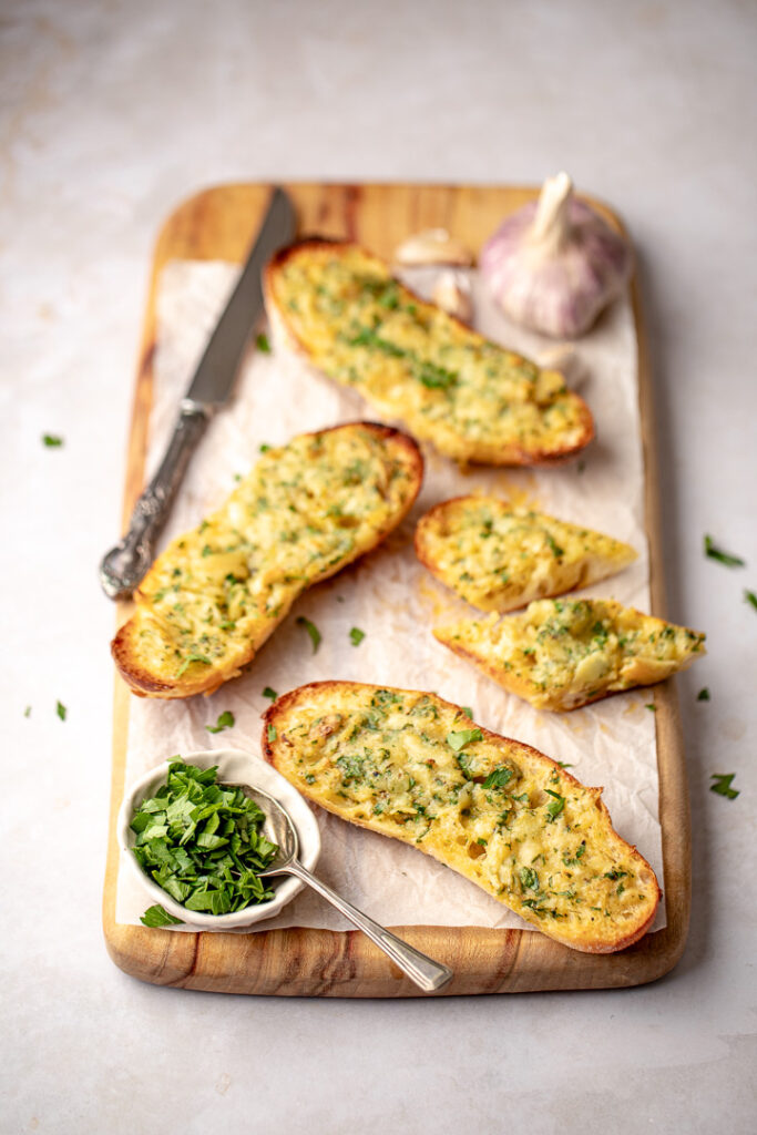 A wooden board with pieces of cheesy roasted garlic bread on top