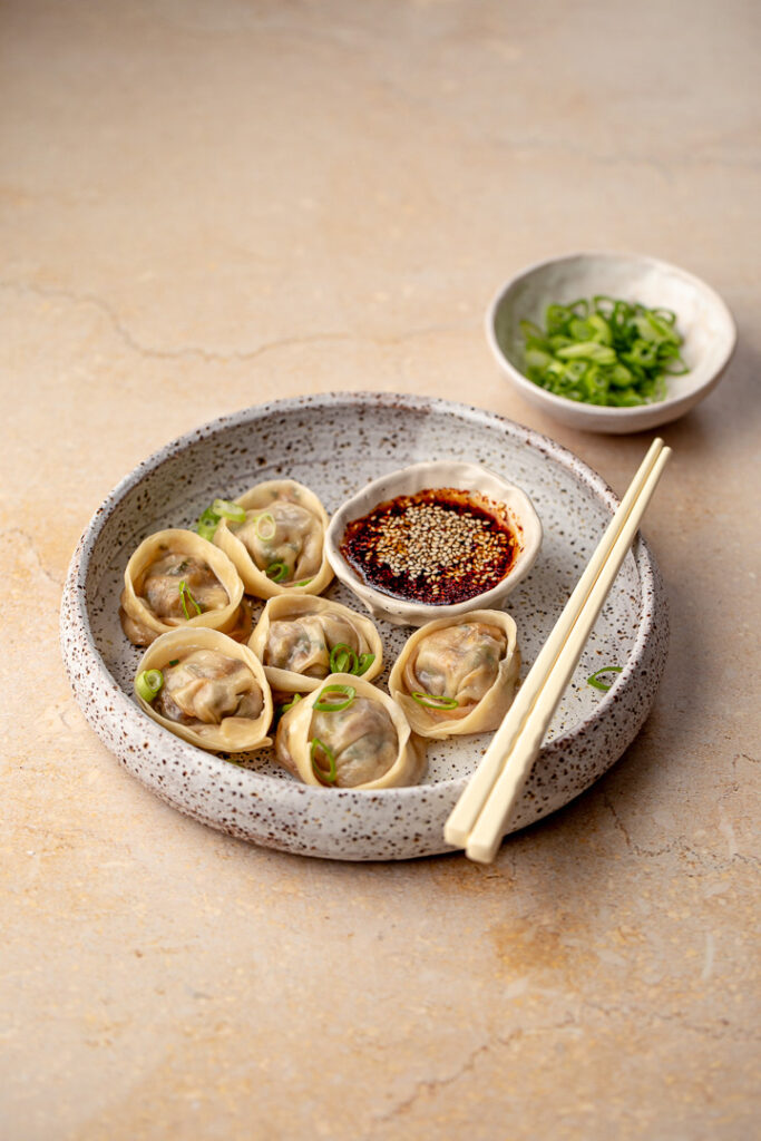 A plate of beef and kimchi mandu with dipping sauce and chopsticks 