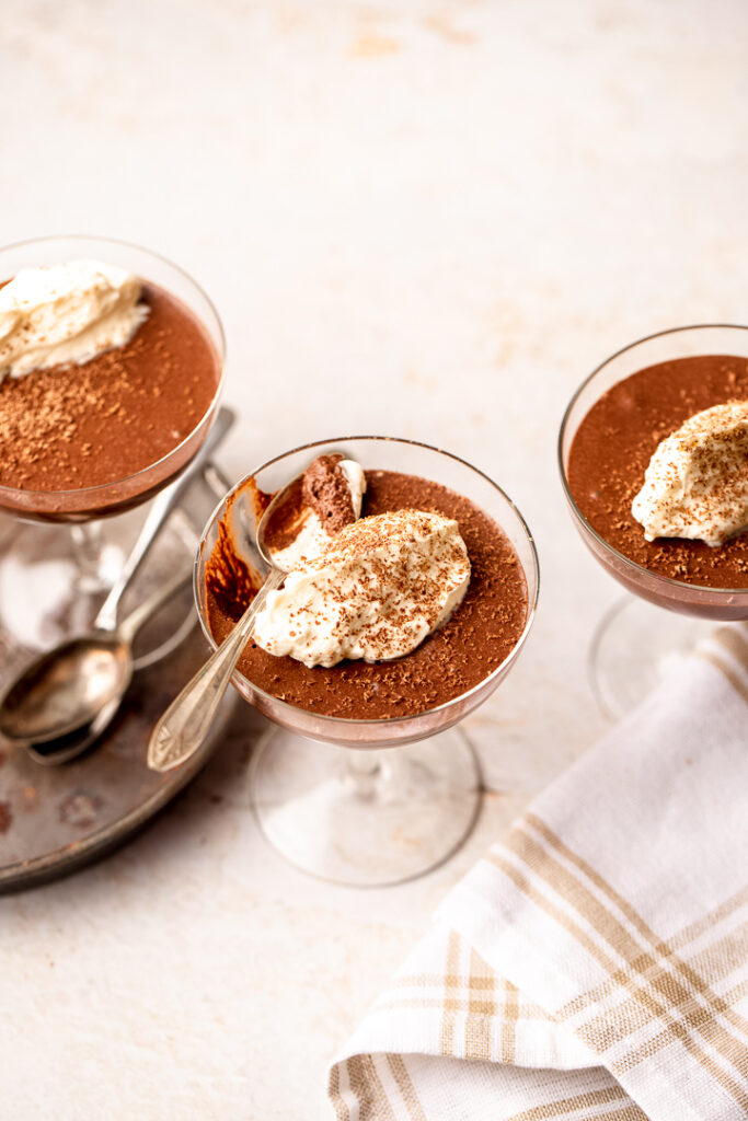Three coupe glasses filled with chocolate mousse, dolloped with cream on top.