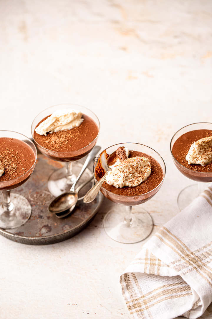 Four coupe glasses filled with chocolate mousse, dolloped with cream on top.