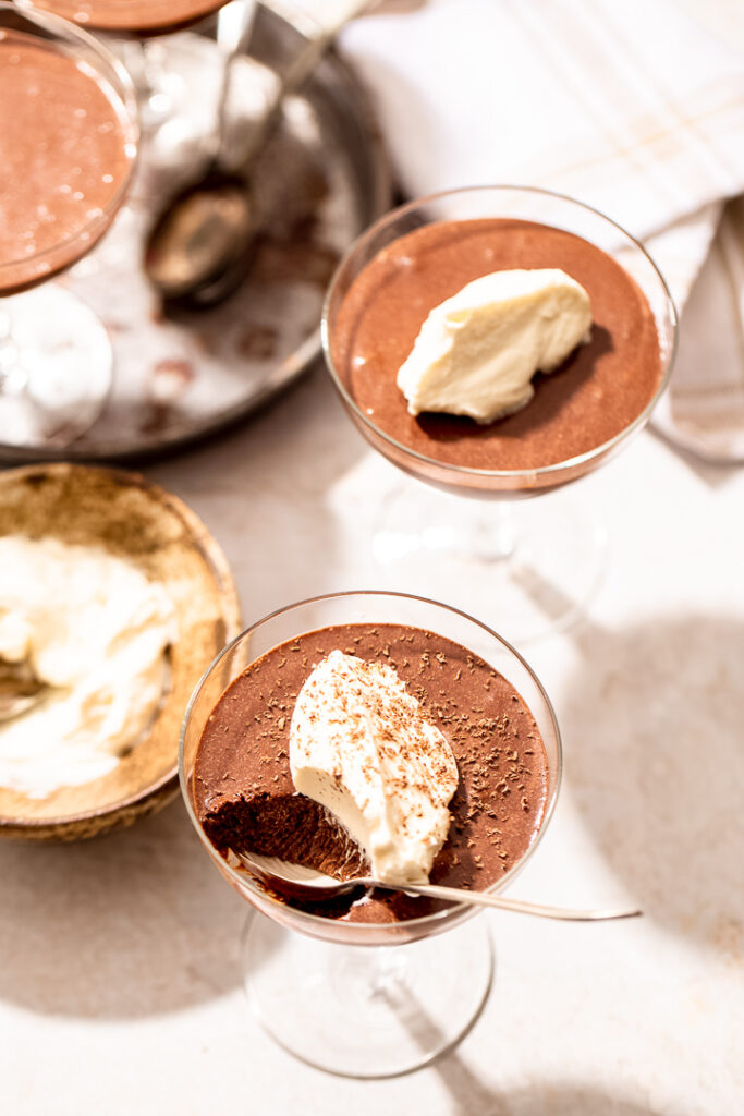 A coupe glass with chocolate mousse. A teaspoon rests on the edge with a scoopful of mousse taken out.