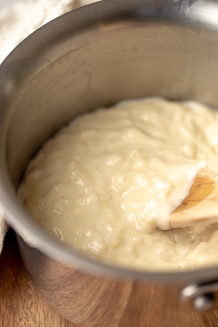 Creamy coconut rice pudding in a pot with a wooden spoon resting in it.