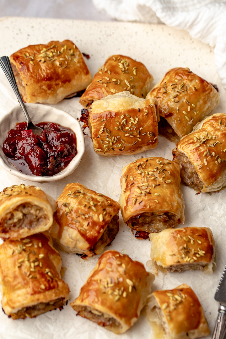 Pork and apple sausage rolls on a white tray, next to a small bowl of tomato relish