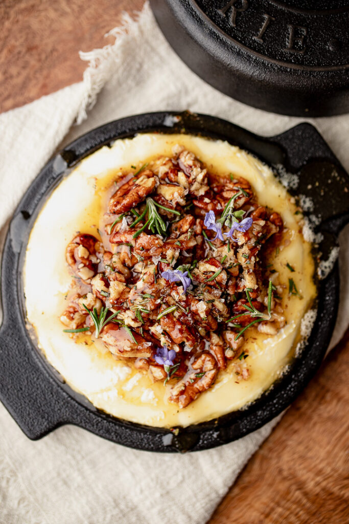 Baked brie with pecans, honey and rosemary in a black dish