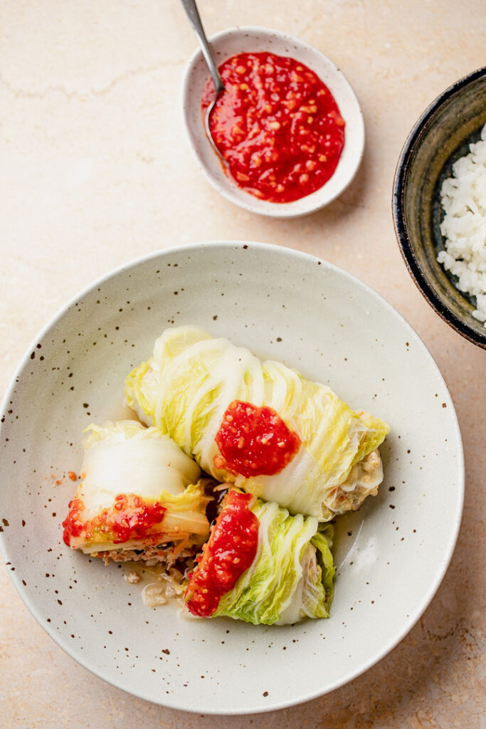 A bowl with two cabbage rolls, one cut in half. Topped with sambal.