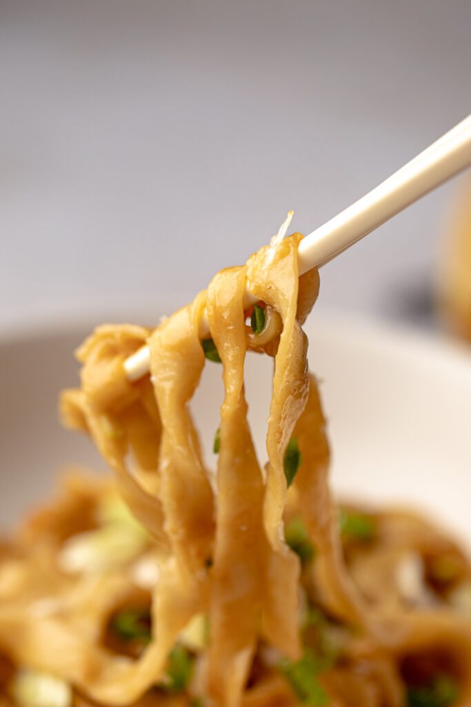 Chopsticks lifting out knife-cut noodles coated with garlic oyster sauce 