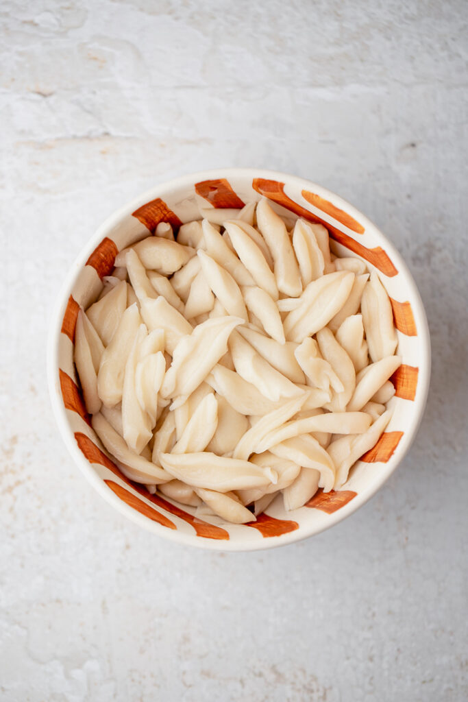 An orange and white striped bowl filled with cooked scissor-cut noodles