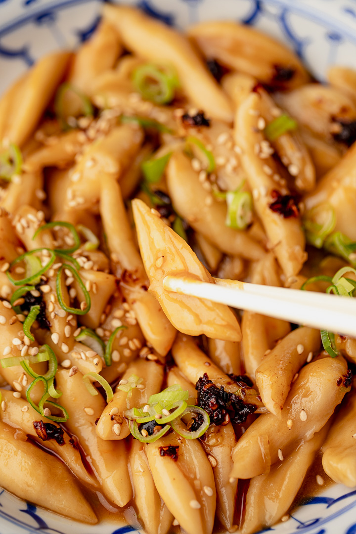 A close up of Garlic Oyster Sauce Scissor-Cut Noodles. Chopsticks picking up one noodle.