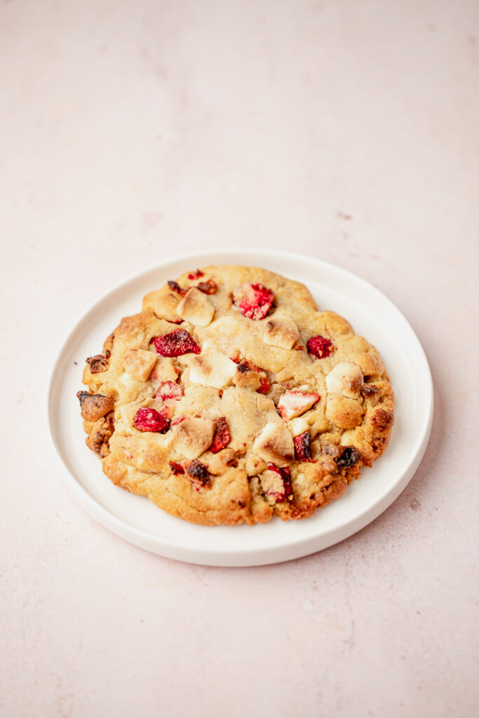 A large strawberry and white chocolate cookie for two on a while plate