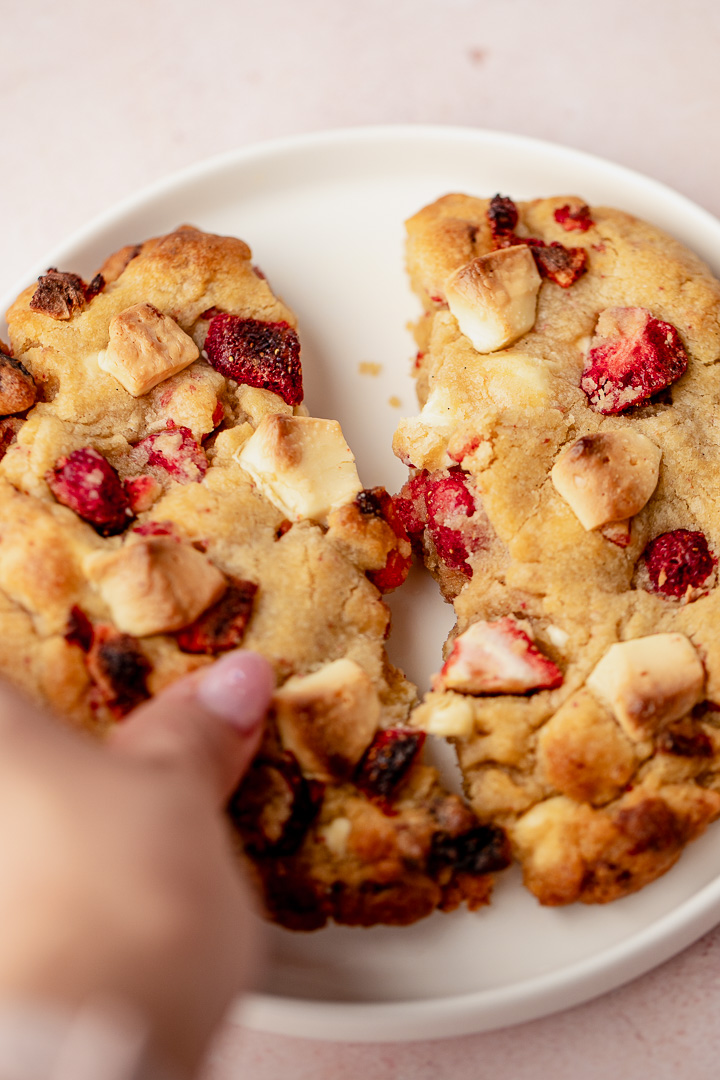 A hand breaking a cookie in half on a white plate