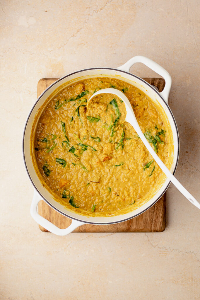 A top down shot of a pot with a ladle in it, with pumpkin coconut dal