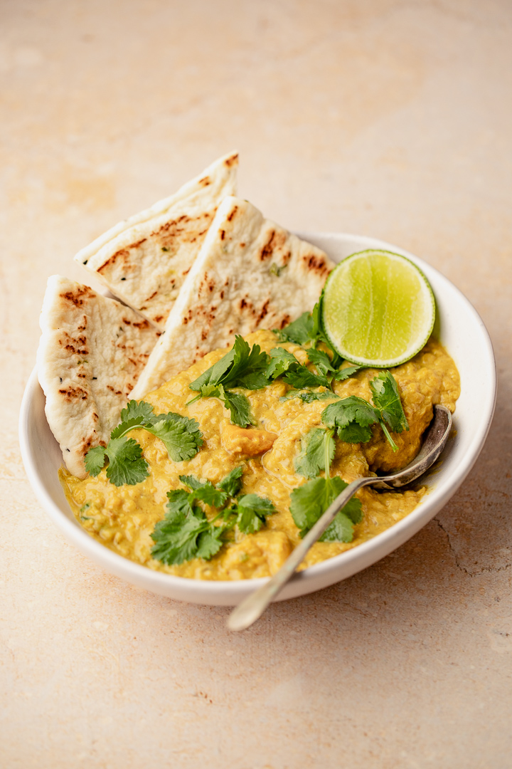 A bowl of pumpkin coconut dal, naan flat breads and a wedge of lime